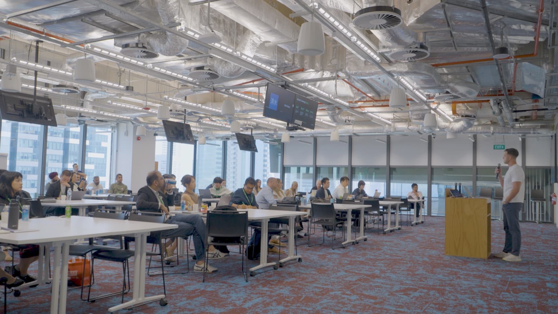 Wide shot of Jordan delivering the AdFuse keynote at Meta HQ Singapore - audience seated at desks, Jordan presenting on the right with a microphone